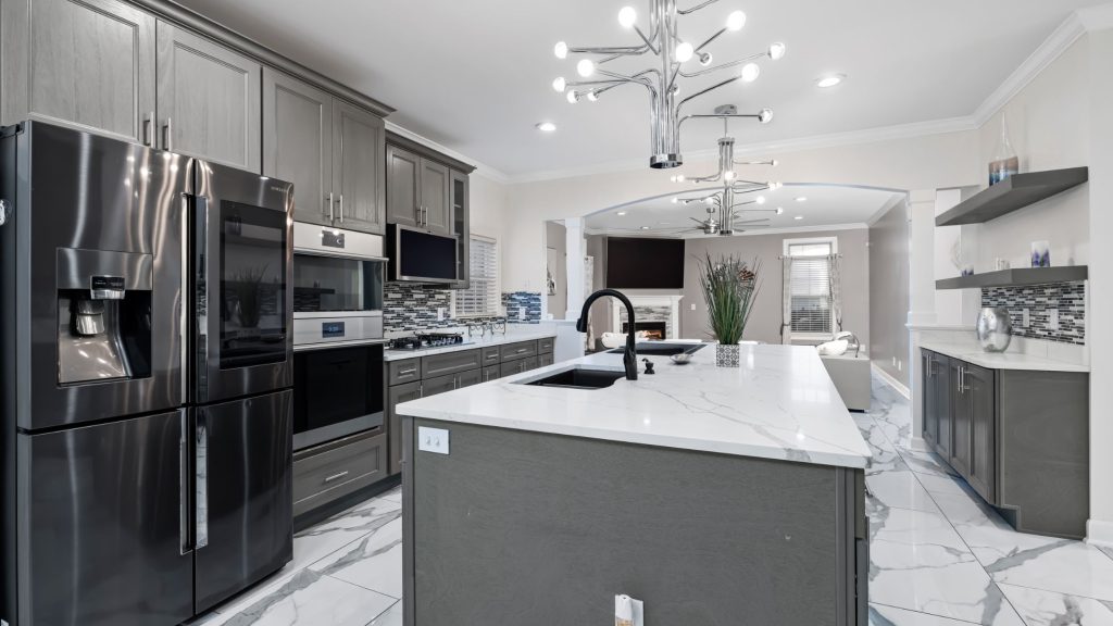Kitchen with gray cabinets, black stainless appliances, white veined island with black faucet and chrome chandelier