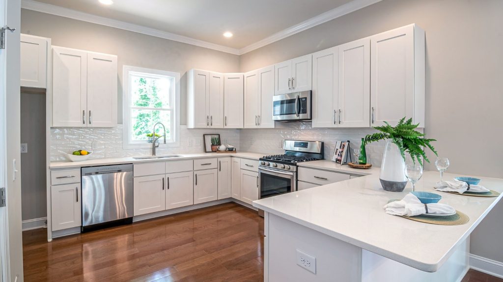 Kitchen with white shaker wall and base cabinets, stainless steel appliances, white peninsula counter and dark wood floor