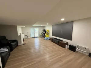Long finished basement in Natick, MA with wood-look plank floor, large projector screen, recliners and arcade machines