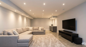 Finished basement living room with a gray sectional sofa, shag rug, wall-mounted TV, concrete floor and recessed lights