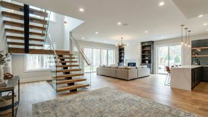 Bright open living space with a floating wood staircase, sectional sofa, fireplace and kitchen island