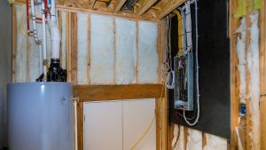 Framed basement utility wall with white batt insulation, an open electrical panel and a gray water heater